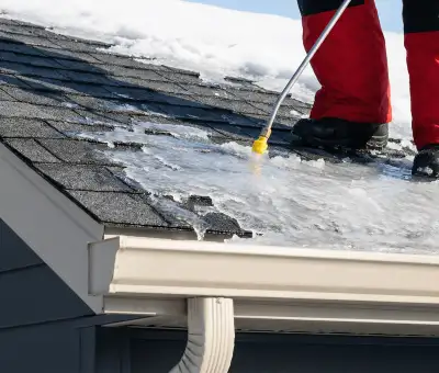 Ice dam removal technician using a steam wand to melt thick ice buildup on a residential roof in Stamford, CT