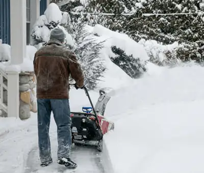 Residential snow removal technician using a snow blower to clear a home driveway and walkway in Stamford, CT