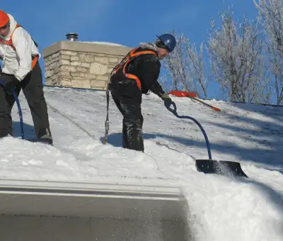 Professional technicians performing roof snow removal with safety harnesses and shovels in Stamford, CT
